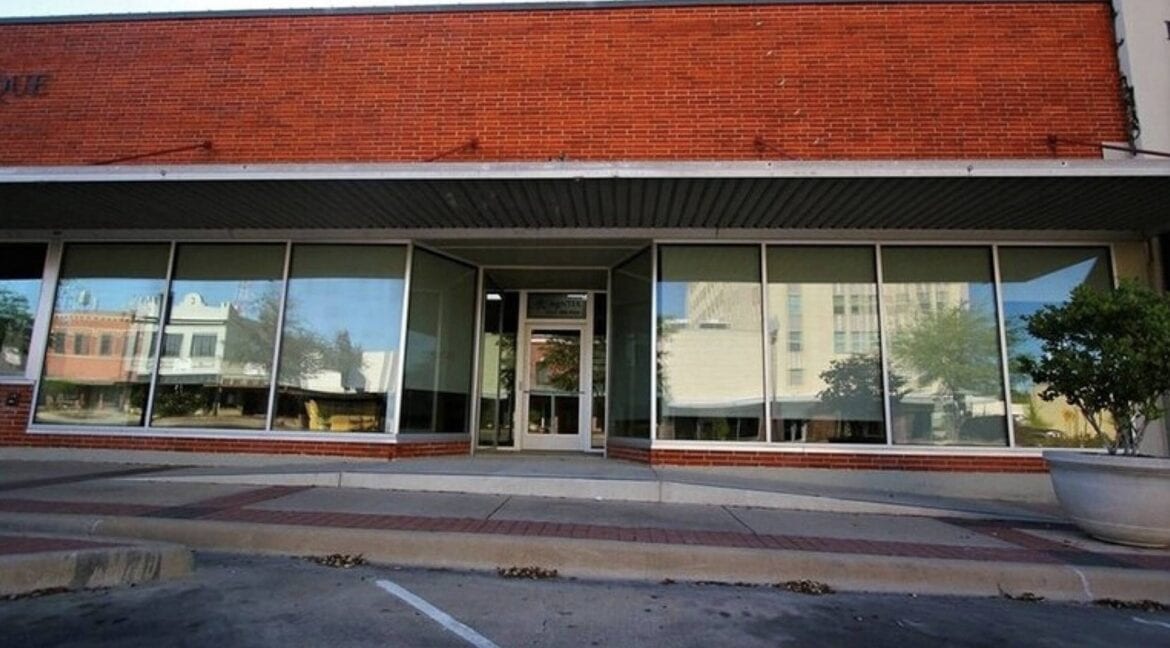 Empty commercial storefront with large glass windows and a brick facade in Bryan, Texas.